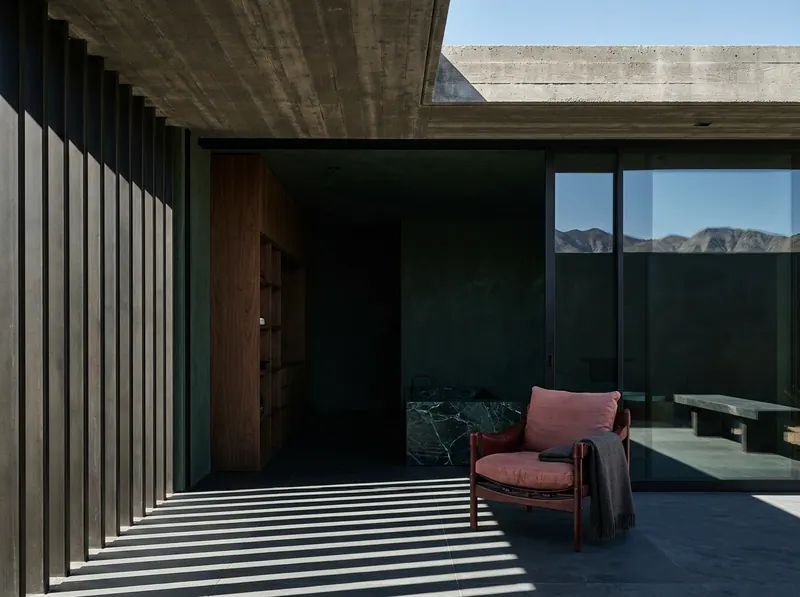 Interior design Palm Springs — a Coachella Valley desert residence in deep forest green with brise-soleil shadow across honed slate and a shaded stone terrace, by Beverly Hills Luxury Interiors