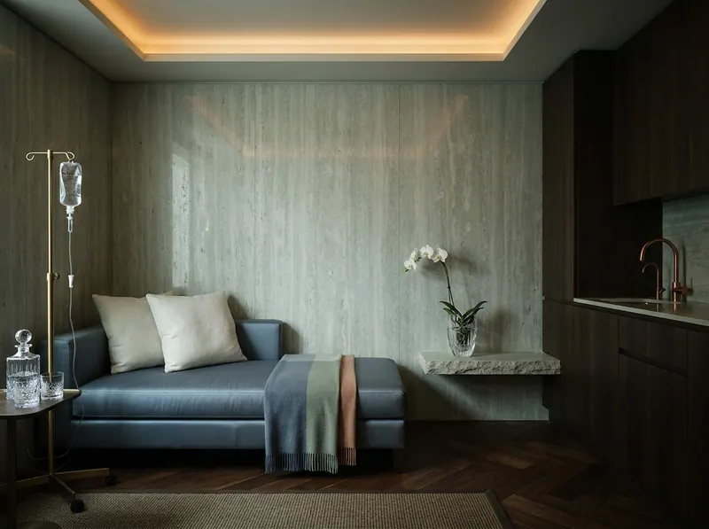 Ultra-luxury Pharisas recovery suite, slate blue silk daybed, grey-green travertine walls, dark walnut herringbone floor, crystal glass vessel with white orchid — Pharisas longevity home design by Beverly Hills Luxury Interiors